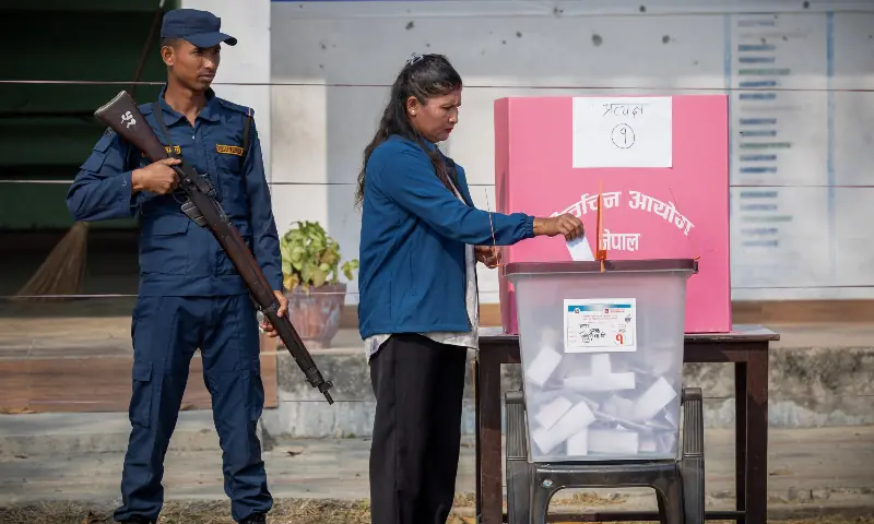 A woman casts her vote as a security officer stands guard at a polling station at a village, in Jhapa district, Nepal on March 5, 2026. &mdash; Reuters