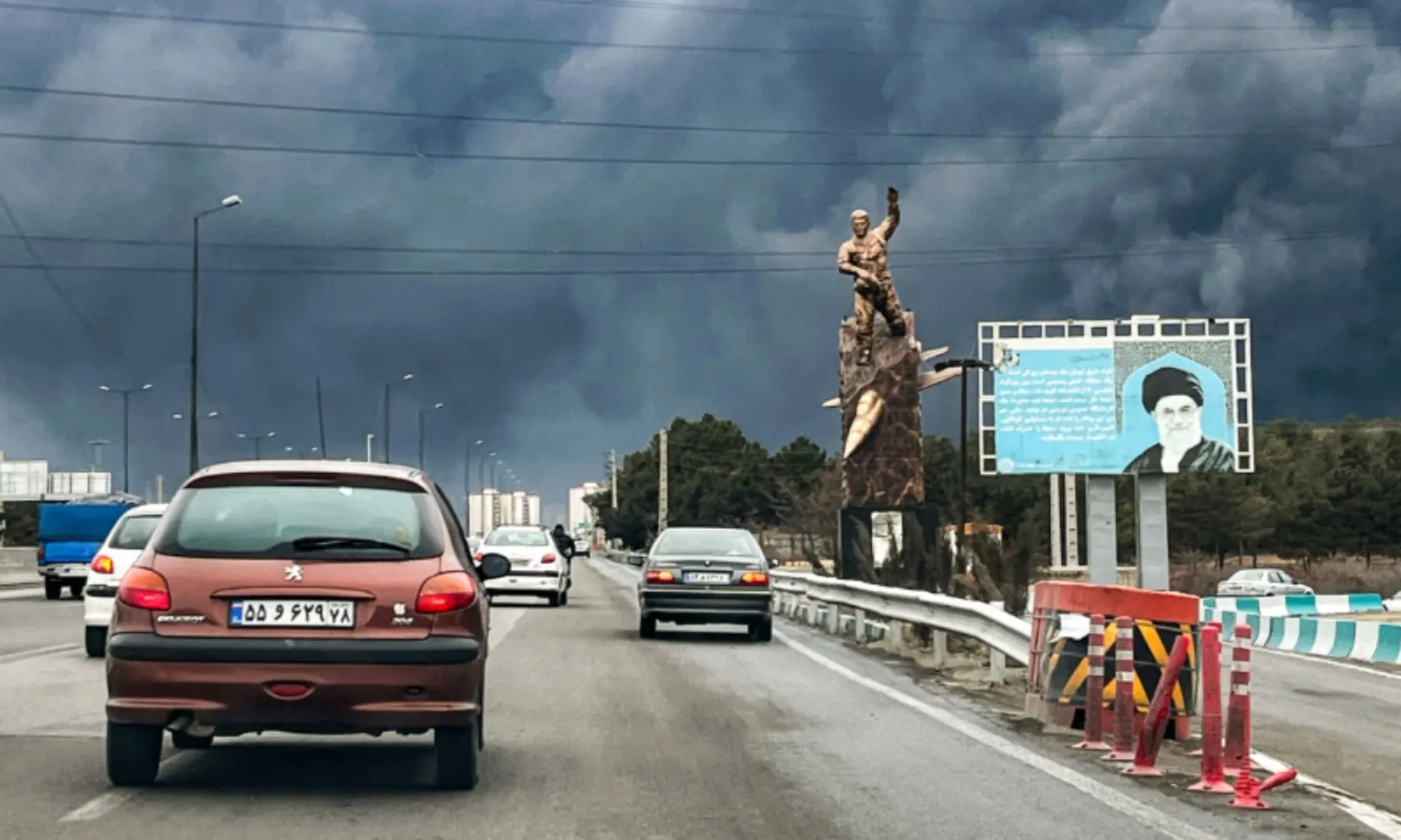 Vehicles move along a highway past a war memorial statue and a billboard depicting Iran&rsquo;s late supreme leader Ayatollah Ali Khamenei, who was assassinated in an air strike on February 28, with plumes of black smoke billowing, in Tehran on March 8, 2026. &mdash;AFP