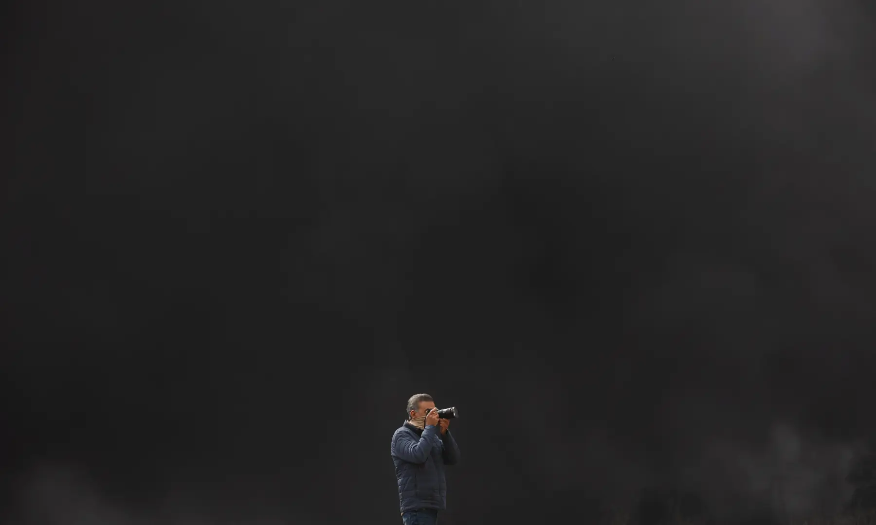 A photographer takes pictures as smoke rises after a reported strike on Shahran fuel tanks on March 8, 2026. &mdash; WANA via Reuters