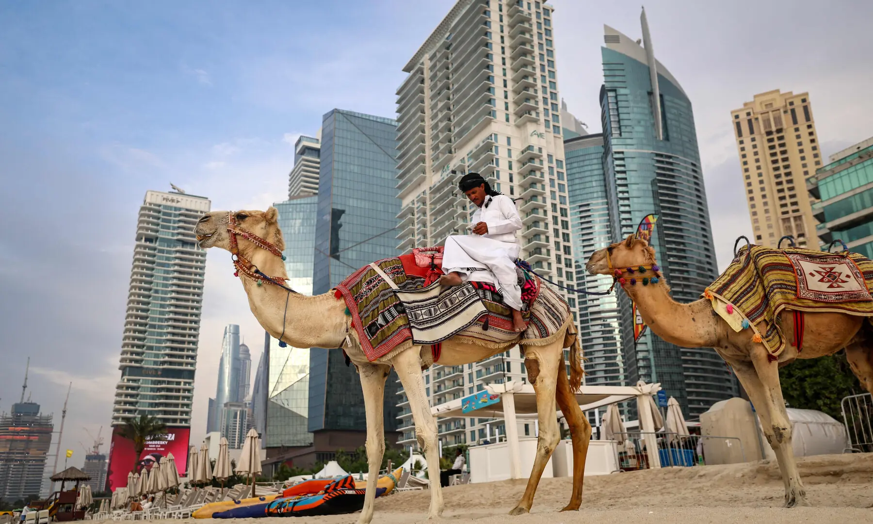 A cameleer checks his phone while sitting on his camel on the beach in Dubai on March 10, 2026. &mdash; AFP