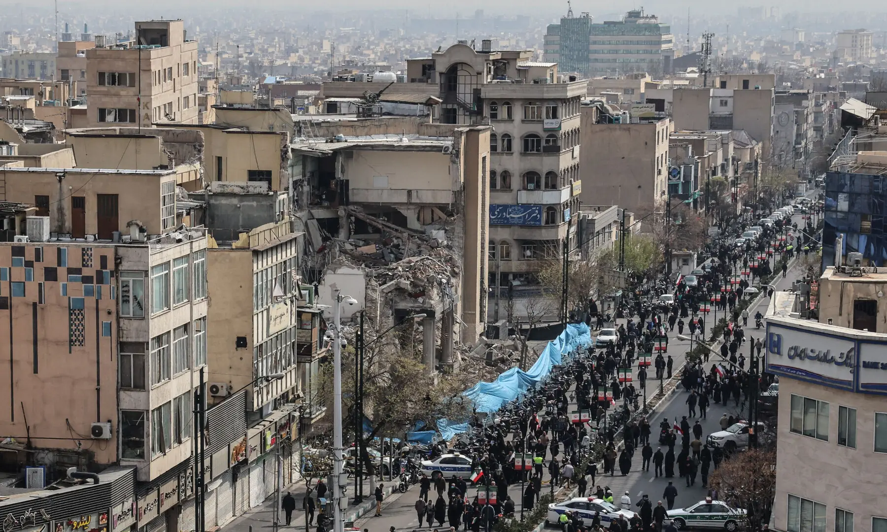 Iranians walk past a damaged building as they attend the funerals of Iran&rsquo;s Revolutionary Guards Corps (IRGC) commanders, army commanders and others killed in the early days of the United States and Israeli strikes on Iran, at Enghelab Square in Tehran on March 11, 2026. &mdash; AFP