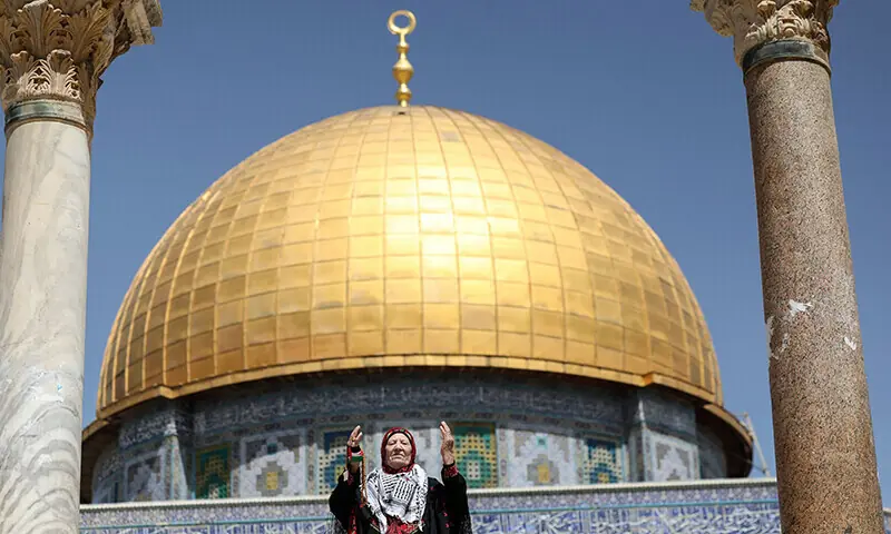 A Palestinian woman dressed in a traditional embroidered dress raises her arms in prayer as she stands in front of the Dome of the Rock mosque in Jerusalem during the last Friday prayer of Ramazan on April 5, 2024. &mdash; AFP/FIle