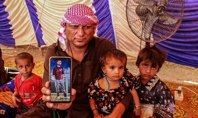 Abdul Malick (2L), a transporter and uncle of Pakistani national Muzaffar Ali, who was killed in Dubai amid the ongoing Middle East war, displays a picture of Ali on his cell phone, after funeral in Jamshoro in Sindh province on March 12. &mdash; AFP
