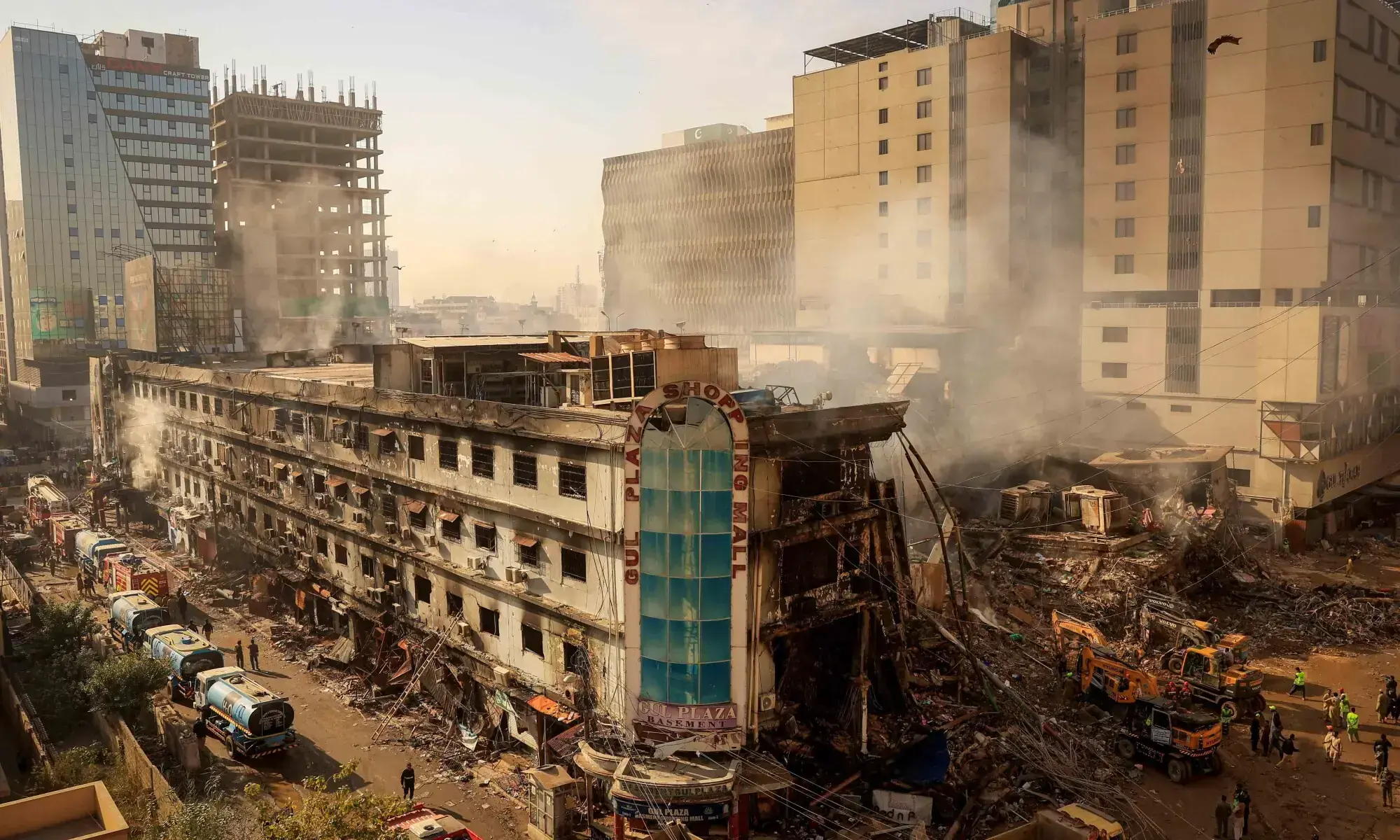 Fire department and municipal workers stand near the site, following a massive fire that broke out in the Gul Plaza Shopping Mall in Karachi on January 20, &mdash; Reuters/File