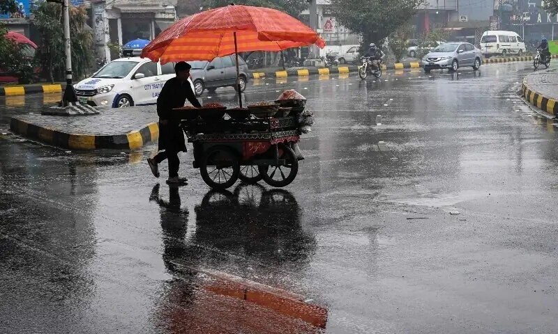 A vendor pushes his food cart as he walks across a road during rainfall in Lahore on December 27, 2024.  &mdash; AFP/File