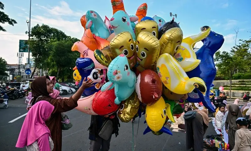 A Muslim woman with her child buys a ballon after offering Eidul Fitr morning prayer along a road in Surabaya, Indonesia on March 20, 2026. &mdash; AFP