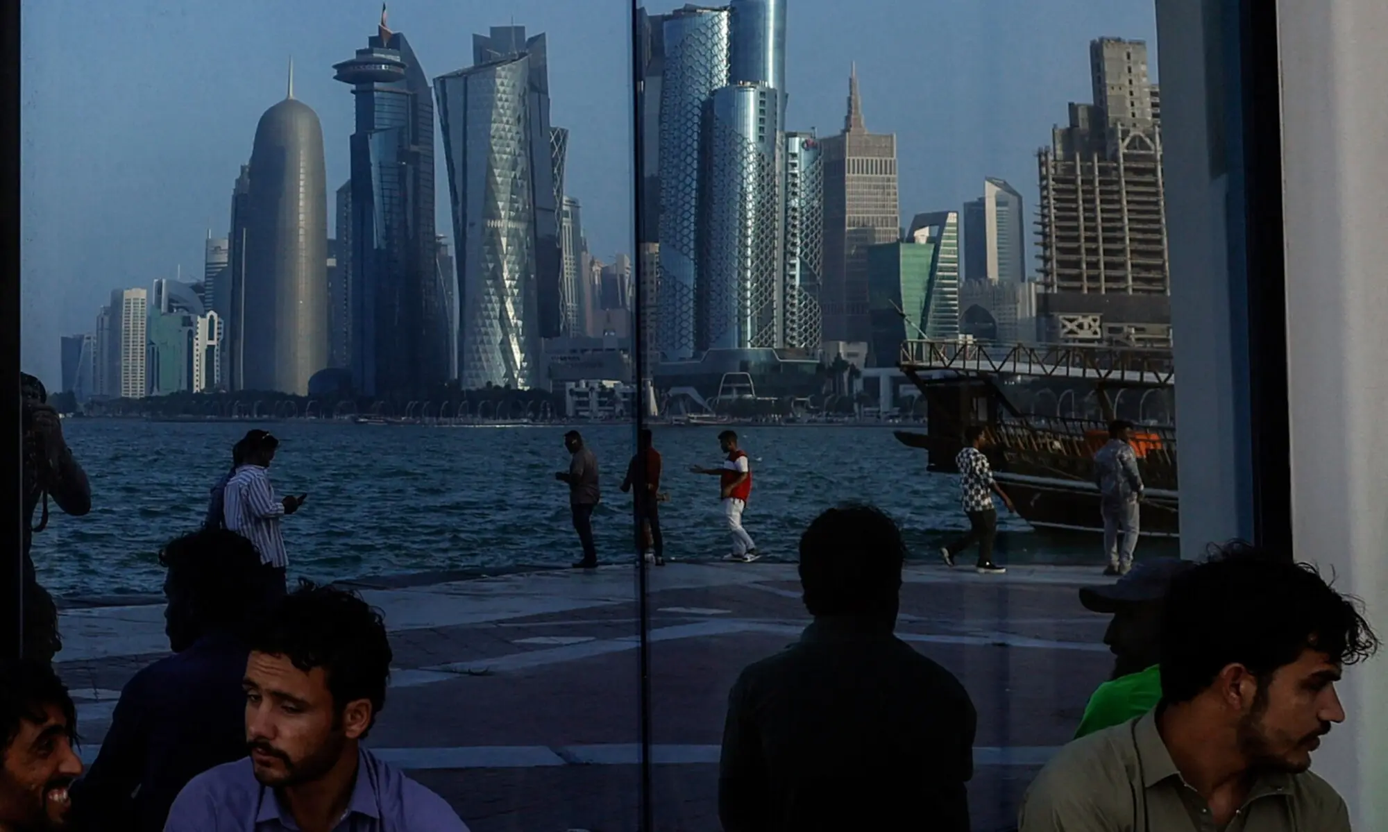People sit with the reflection of the Doha skyline along the Doha Corniche, on the second day of Eidul Fitr in Doha on March 21, 2026. &mdash; AFP