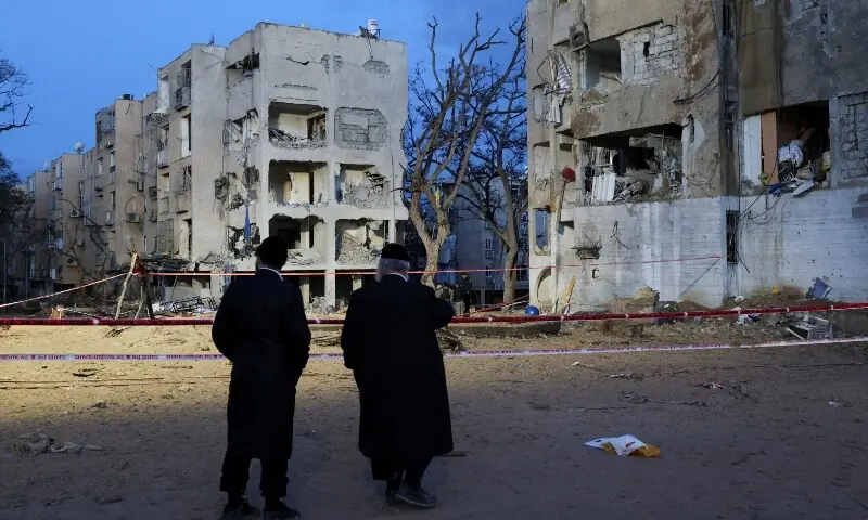 People stand at the scene of damage after Iranian missile barrages struck residential buildings in Arad, amid the US-Israel conflict with Iran, in southern Israel, March 22. &mdash; Reuters
