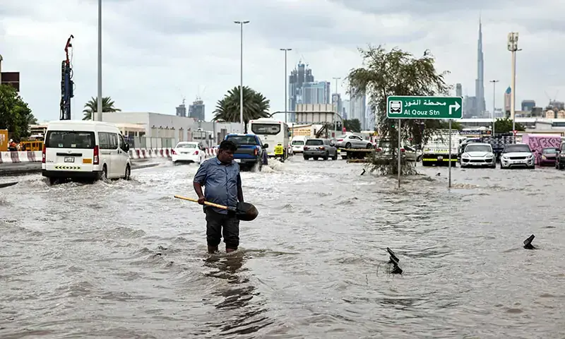 A man wades through flood waters to clear a drain as a street near the Burj Khalifa floods following heavy rains in Dubai, the UAE on December 19. &mdash; AFP