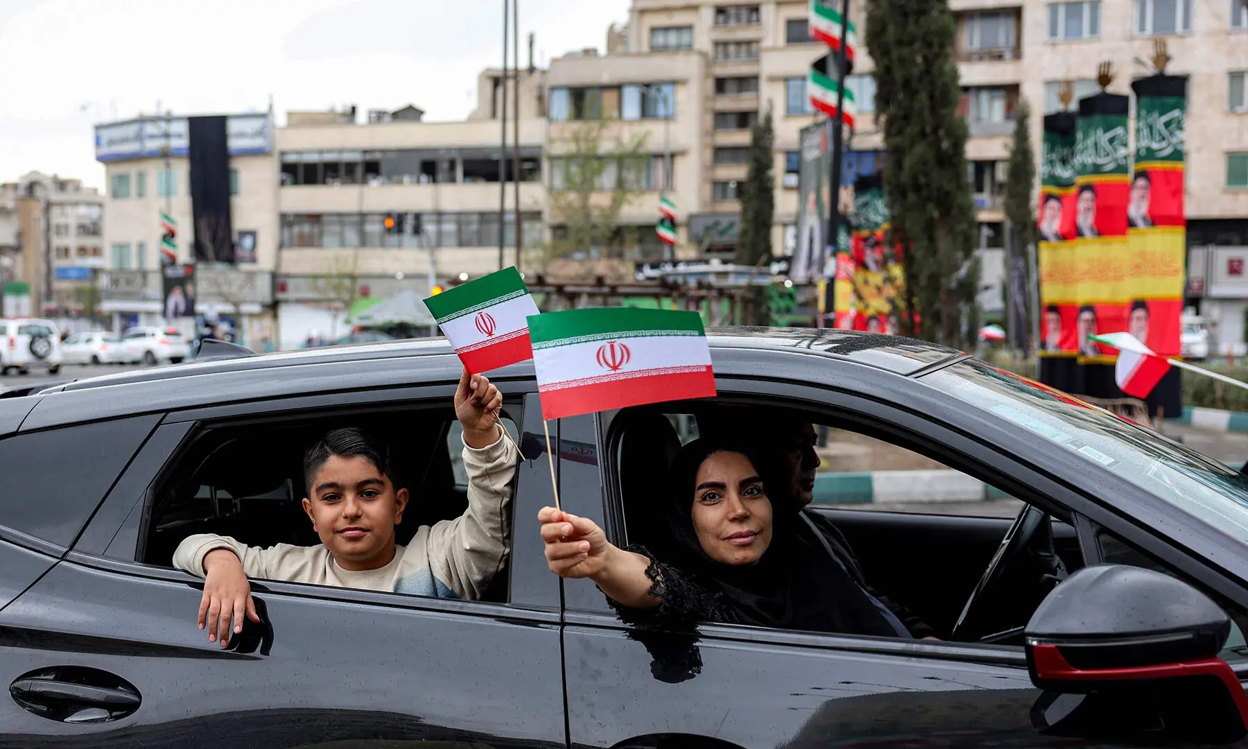 A woman and boy hold up miniature Iranian flags while sitting in a vehicle in Enghelab Square in central Tehran, Iran on March 25. &mdash; AFP