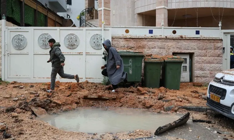 Men run past a crater following a projectile strike in the Arab-Israeli city of Kfar Qassem on March 26, 2026. &mdash;AFP