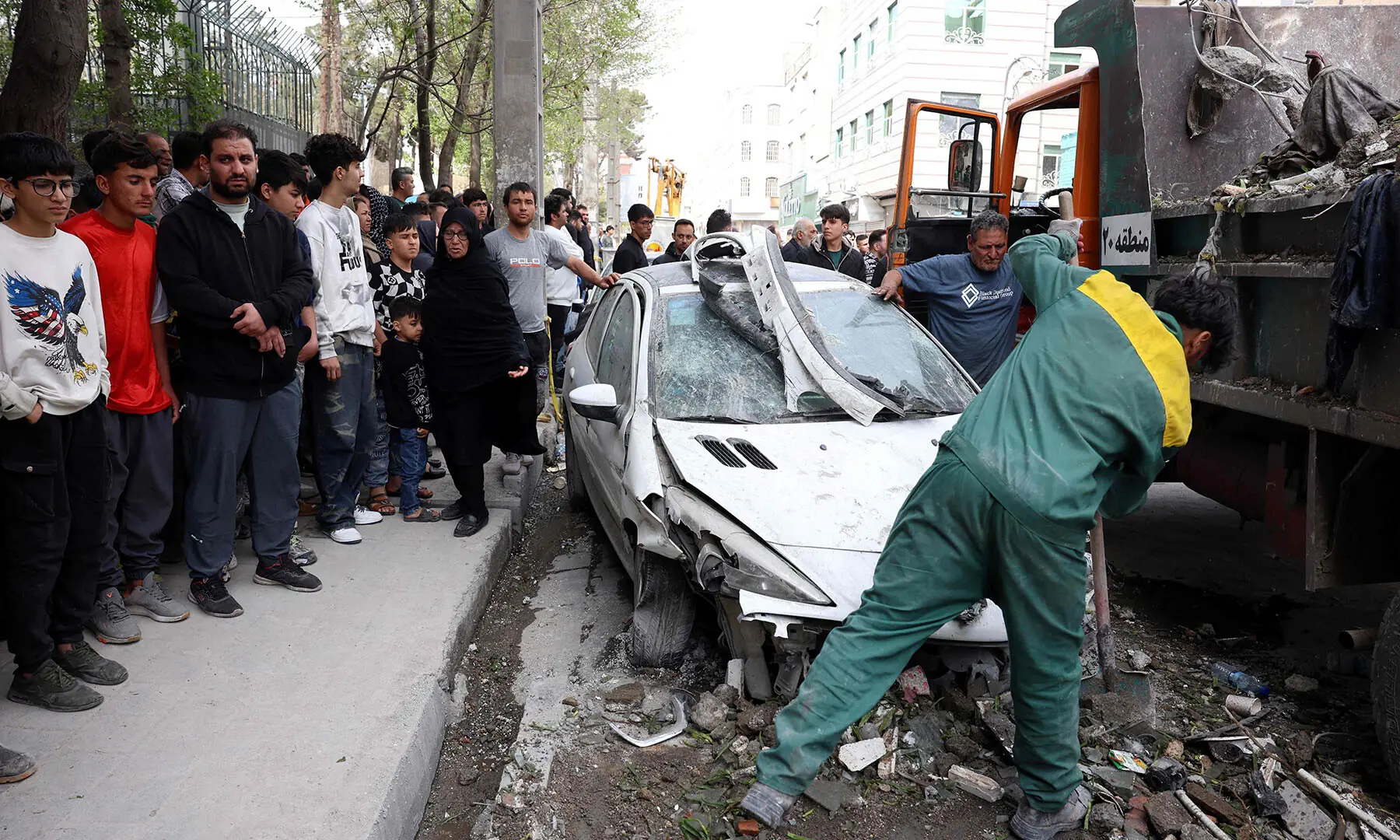 People gather as workers remove the wreckage of a car outside a residential building that was targeted in southern Tehran, Iran on March 27. &mdash; AFP
