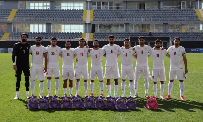 Iran players line up before the match as school bags are laid in memory of the victims of the girls school bombing in Minab, Iran, March 27, 2026. &mdash; Reuters