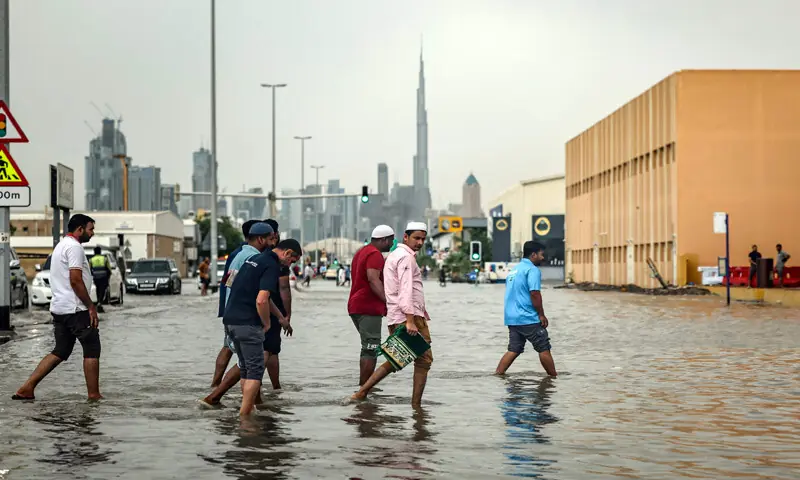 People cross a flooded street after heavy rains in Dubai.&mdash;AFP