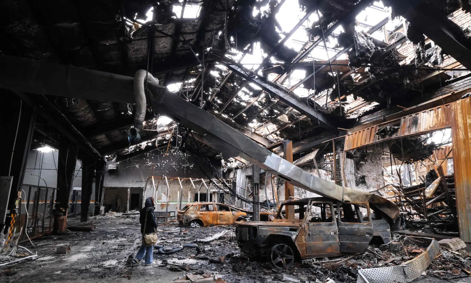 A journalist stands next to the wreckage of a vehicle during the visit of a car service centre in eastern Tehran that was hit by a missile strike, on March 28, 2026. &mdash; AFP
