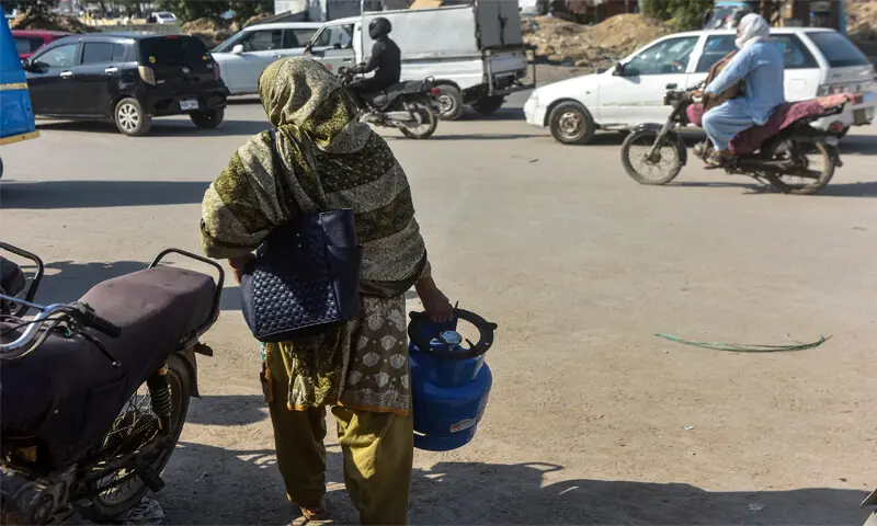 A woman carrying a burner-fitted LPG cylinder walks past a motorcycle in the city.—Fahim Siddiqi / White Star A woman carrying a burner-fitted LPG cylinder walks past a motorcycle in the city.—Fahim Siddiqi / White Star