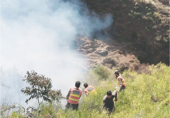 Rescue 1122 workers and locals try to put out a fire in Awarai Puran area of Shangla on Thursday. &mdash; Dawn