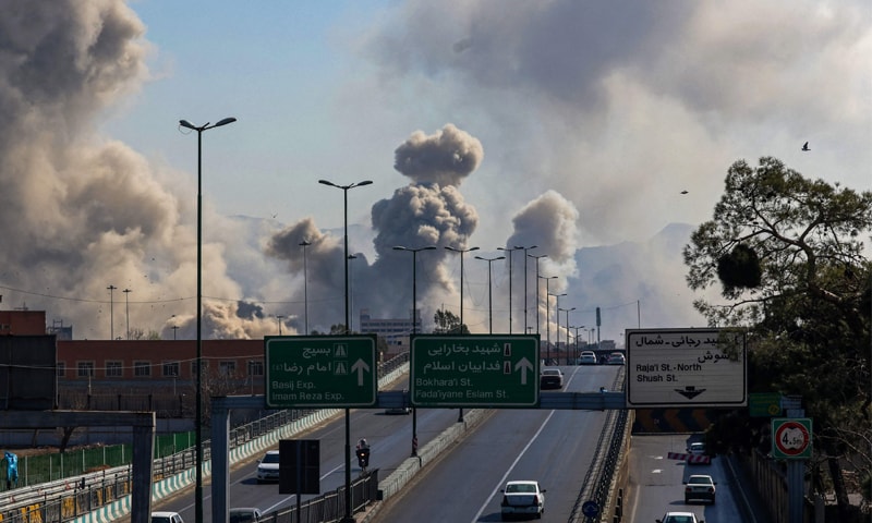 TEHRAN: Plumes of smoke rise after US-Israeli air strikes as motorists drive along an expressway. &mdash;AFP