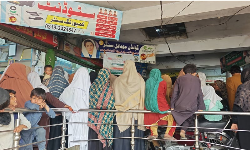 Women wait for their turn at a cash distribution point in Charsadda on Wednesday. &mdash; Dawn