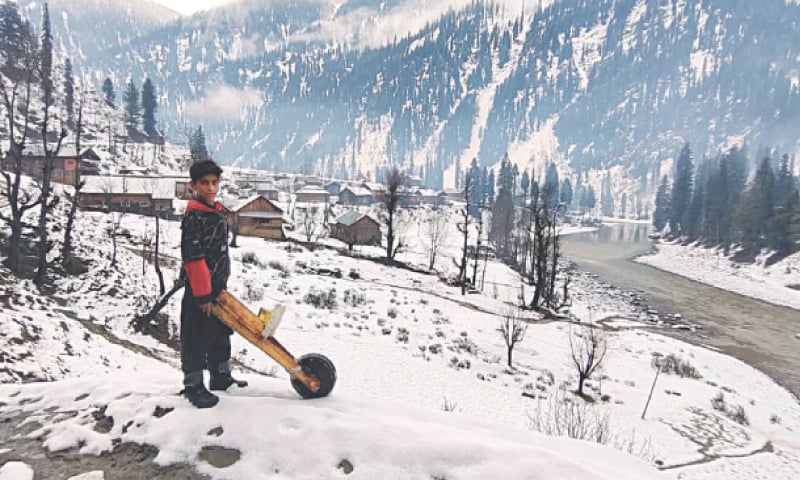 A boy stands with a handmade wooden scooter on a snow-covered slope overlooking the partially frozen Neelum River in Halmat village, in the upper belt of Neelum Valley, Azad Jammu and Kashmir, on Thursday. Snowfall that began on Tuesday night has blanketed Halmat and nearby settlements, covering wooden hamlets, terraced fields and surrounding pine-clad mountains in white bringing the winter chill back across the scenic valley. &mdash; Photo by Tariq Naqash