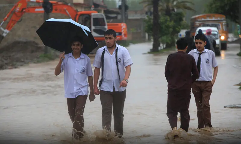 Students wade through rainwater on Warsak Road, Peshawar, on Tuesday. &mdash; White Star