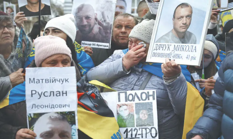A woman wipes her eyes as she stands amongst a group holding photographs of their missing or captured relatives and friends at a prisoner exchange in the Chernihiv region.—AFP A woman wipes her eyes as she stands amongst a group holding photographs of their missing or captured relatives and friends at a prisoner exchange in the Chernihiv region.—AFP