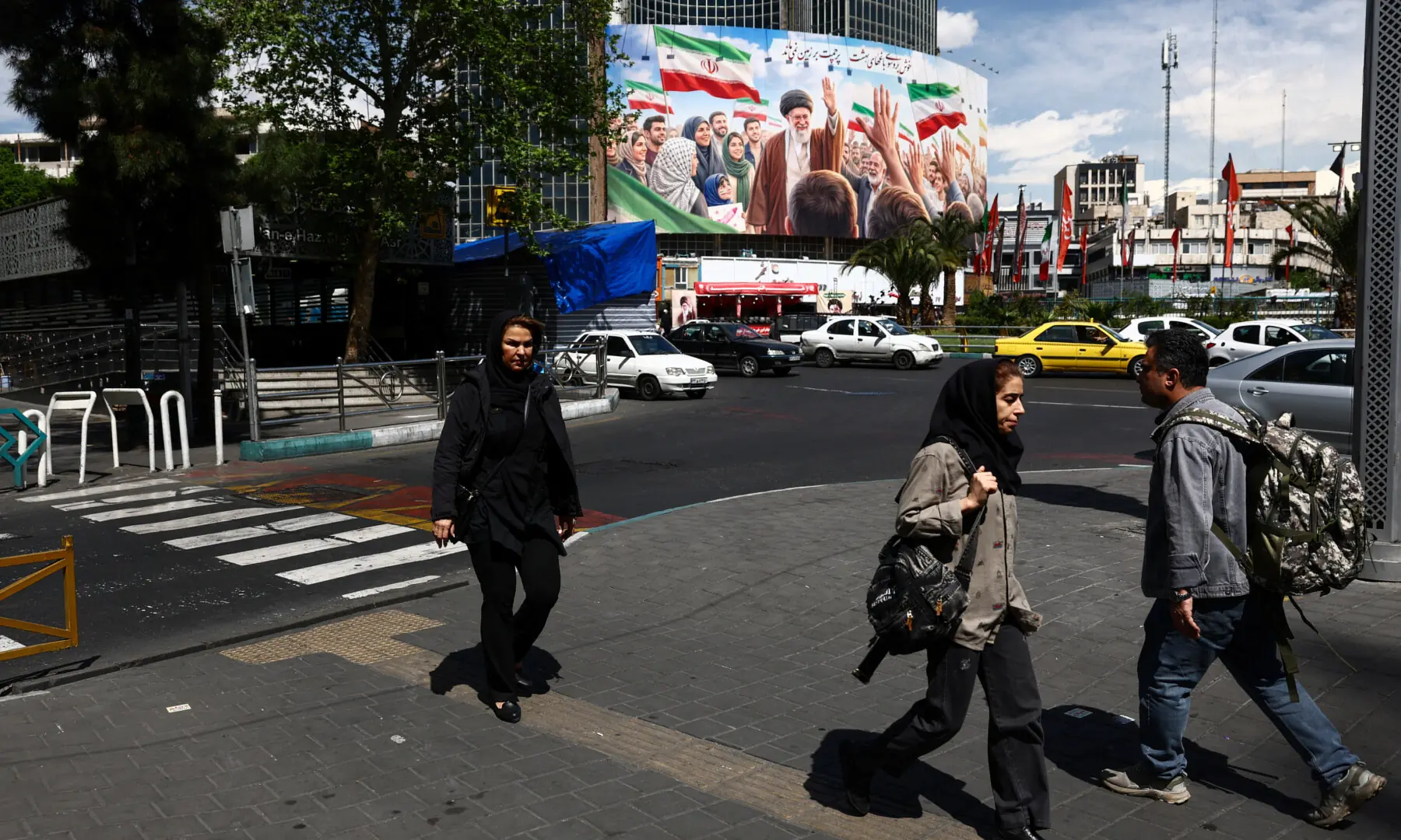 People walk past a billboard featuring an image of the late Supreme Leader of Iran, Ayatollah Ali Khamenei, on a building in Tehran, Iran on April 11, 2026. &mdash; WANA via Reuters