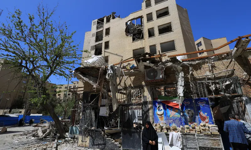 A woman stands next to debris lying in front of a residential building damaged by a strike on March 4, in Tehran on April 14, 2026. &mdash; Reuters