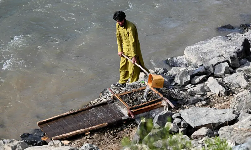 This photograph taken on April 13, 2026 shows an Afghan man pouring water over a seive as he sifts through mountainside stones in search of gold nuggets along the Kunar river in the Song area of Ghaziabad district, Kunar province. &mdash; AFP