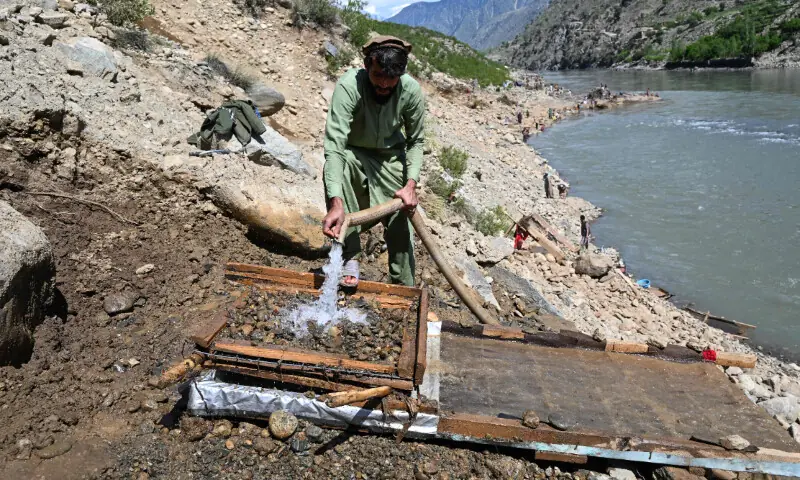 This photograph taken on April 13, 2026 shows an Afghan man pouring water over a seive as he sifts through mountainside stones in search of gold nuggets along the Kunar river in the Song area of Ghaziabad district, Kunar province. &mdash; AFP