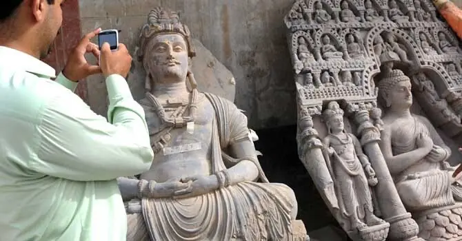A visitor takes photographs on his mobile of seized ancient statues at a museum in Karachi. —AFP A visitor takes photographs on his mobile of seized ancient statues at a museum in Karachi. —AFP