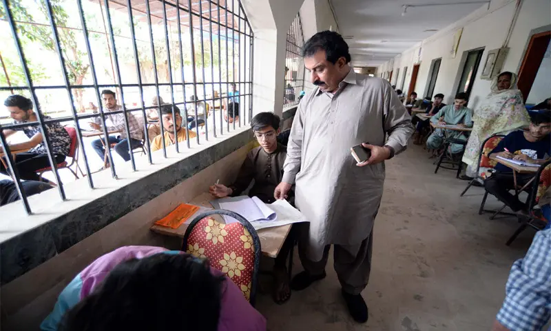 An invigilator checks on students during matric exams at a centre. A large number of students are seated in a corridor without fans during hot weather, while many others are made to sit in the open under the sun.—PPI An invigilator checks on students during matric exams at a centre. A large number of students are seated in a corridor without fans during hot weather, while many others are made to sit in the open under the sun.—PPI
