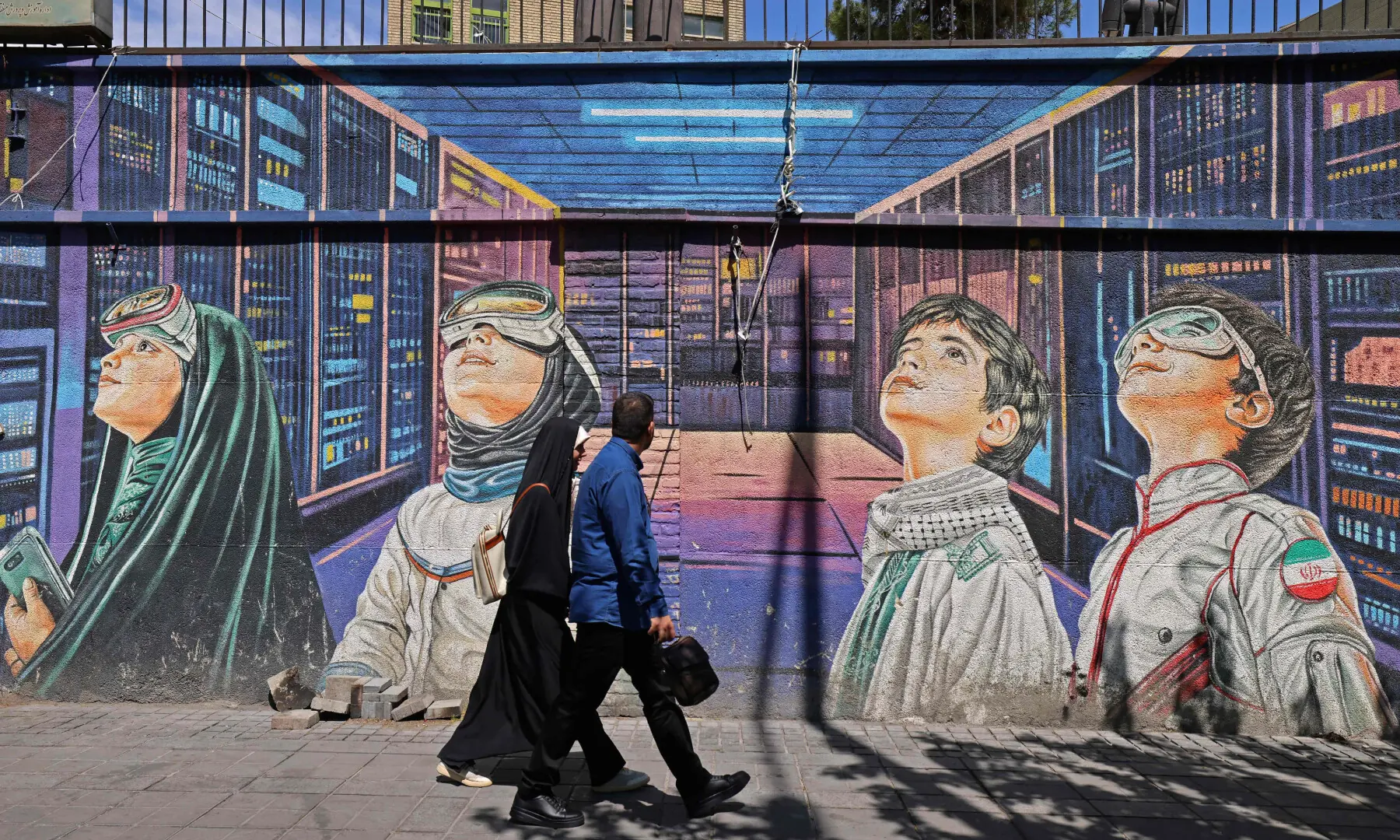 This photo taken on April 12, 2026 shows people walking past a wall mural along the roadside in Tehran. &mdash; AFP/File