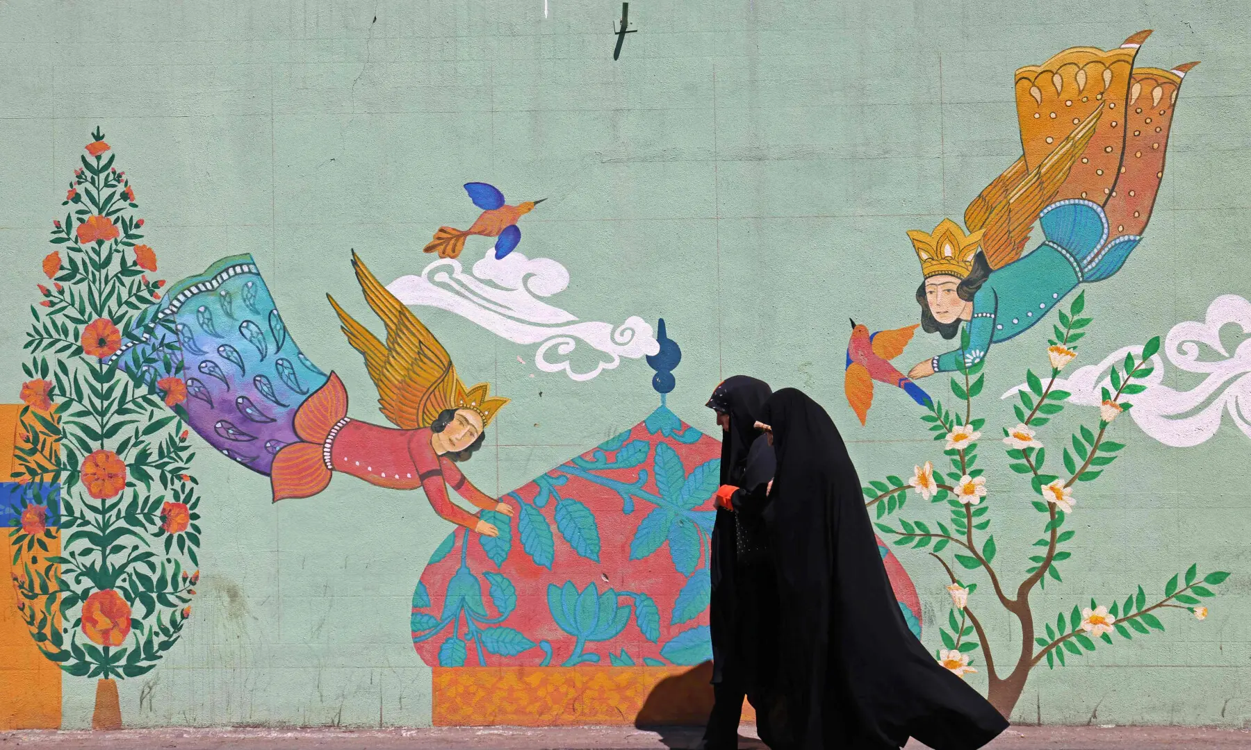 This photo taken on April 11, 2026 shows women walking past a wall mural along the roadside in Tehran. &mdash; AFP/File