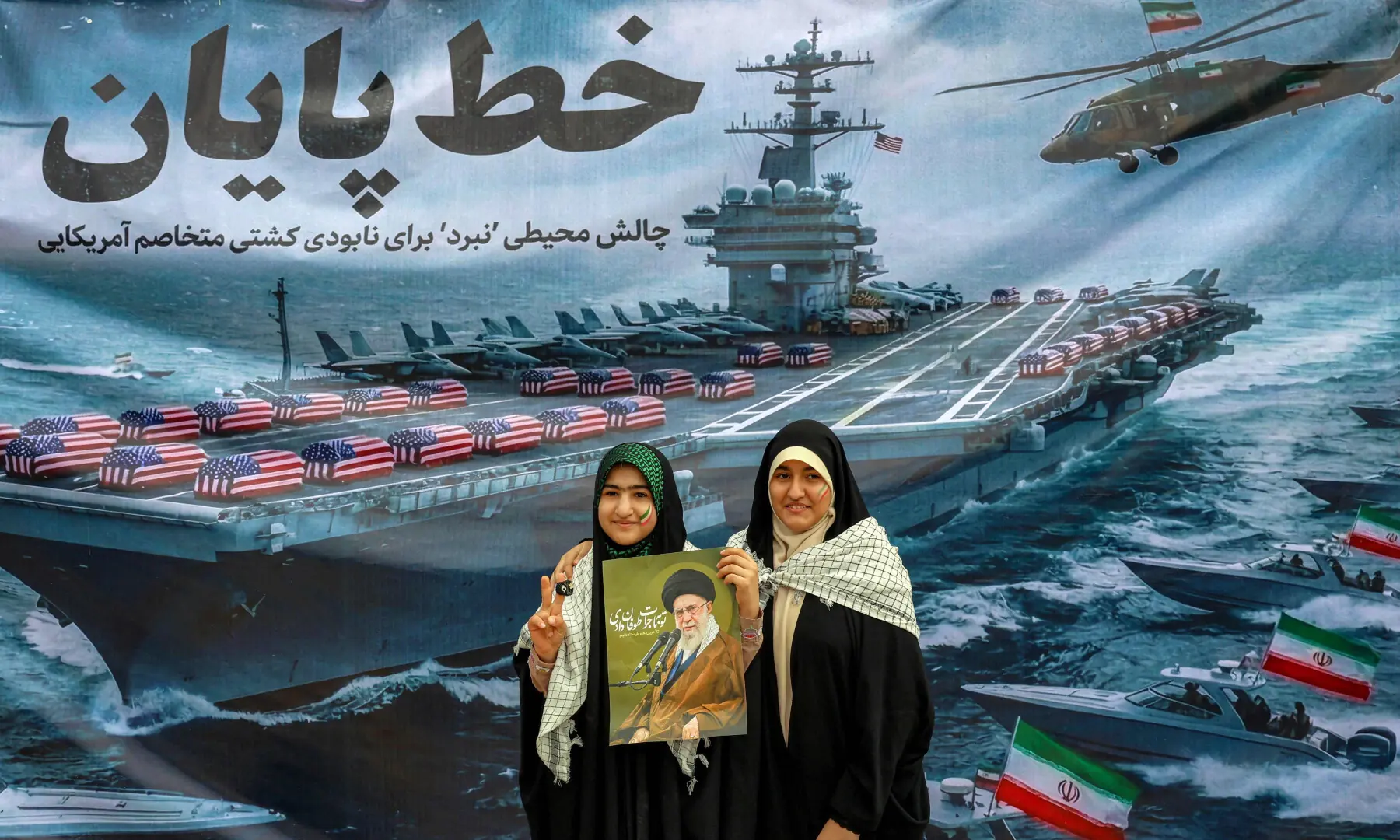 This photo taken on Feb 11, 2026 shows women posing with a poster depicting Iran&rsquo;s supreme leader Ayatollah Ali Khamenei as they stand before a banner depicting a US Navy aircraft carrier with US-flag-wrapped coffins on the deck, during a rally marking the 47th anniversary of the 1979 Islamic revolution in Tehran. &mdash; AFP/File