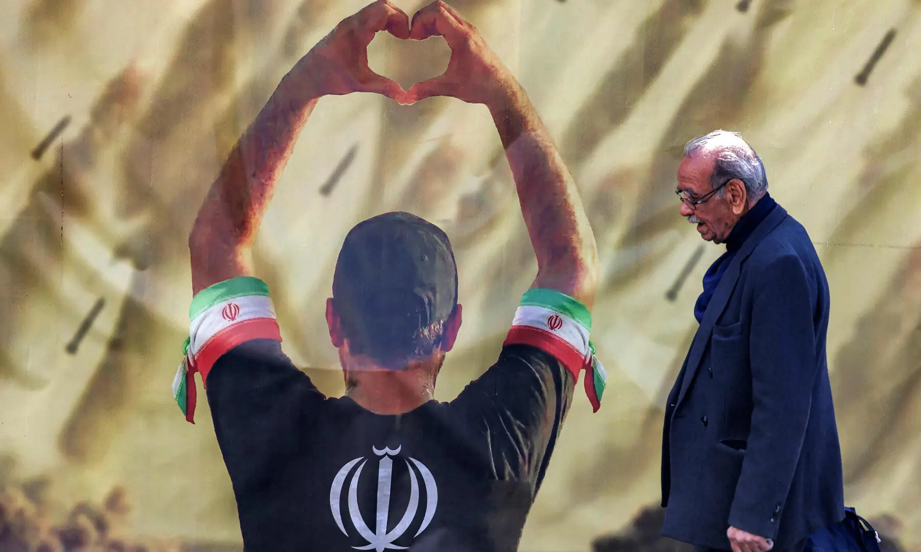 This photo taken on April 6, 2026 shows a man walking past a banner depicting a man holding up a heart gestures before missiles being fired, in Tehran. &mdash; AFP/File