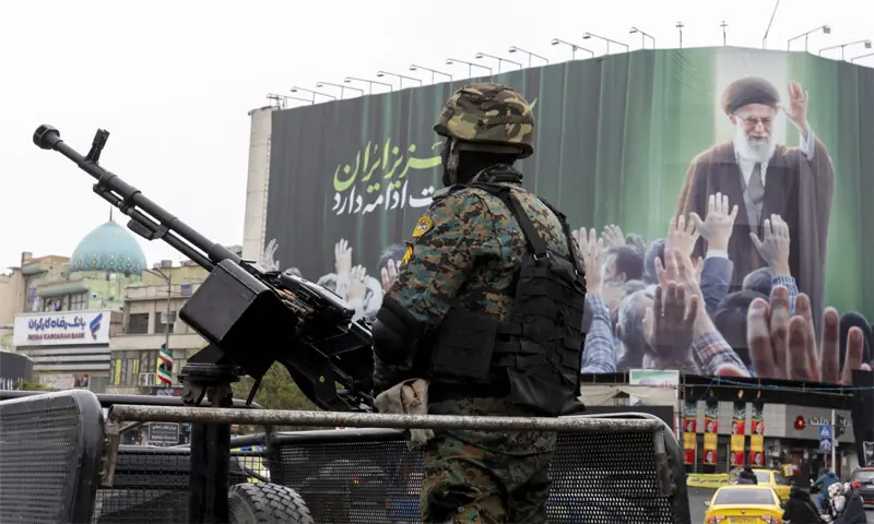 A security personnel member stands guard beneath a poster of Iran's former leader Ayatollah Ali Khamenei in Tehran, Iran on March 10, 2026: Iran&rsquo;s operational strategy has been to fight its own war against the US-Zionist duo, not get into the conflict on America's terms | AFP