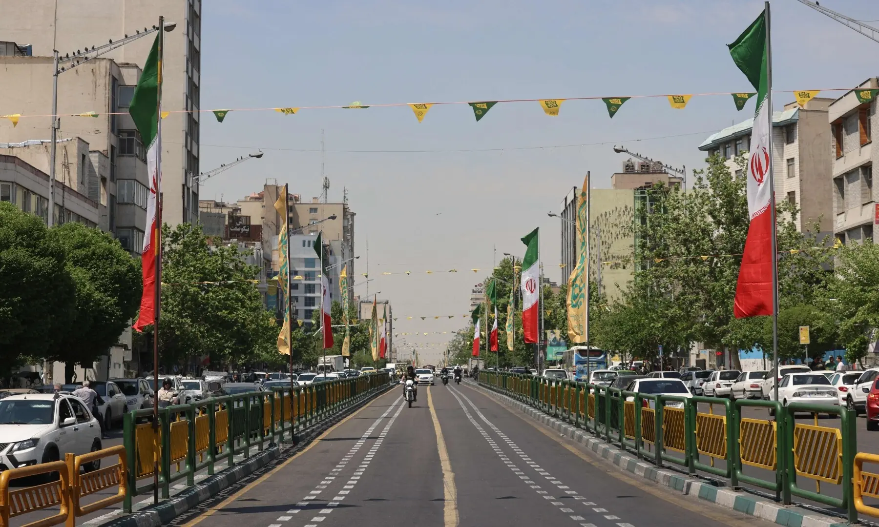 Vehicles and motorbikes drive along a road adorned with Iranian flags in Tehran on April 28, 2026. &mdash; AFP