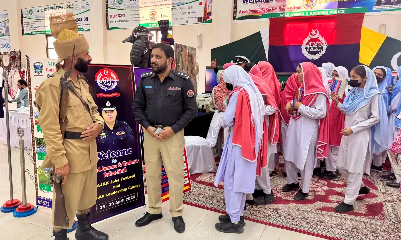 Clad in a pre-partition era uniform of the Jammu and Kashmir Police, a retired AJK police constable speaks with a serving DSP as students visit the AJK Police stall at the Job Festival in Muzaffarabad on Tuesday. &mdash; photo by author