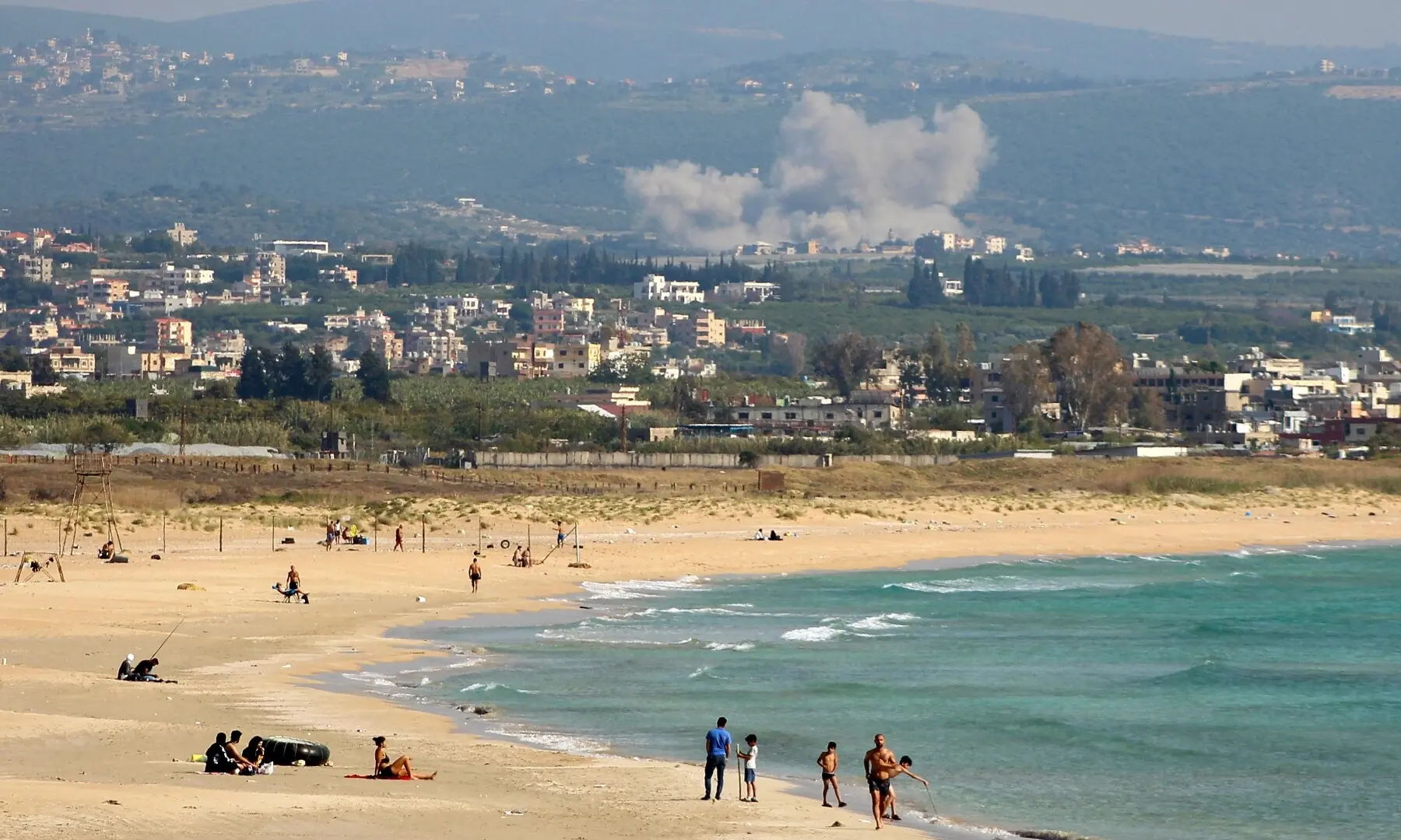 This photograph taken from the southern Lebanese area of Tyre shows people around the beach against the backdrop of smoke rising from the site of an Israeli airstrike that targeted the village of El Qlaile on May 8, 2026. &mdash;AFP