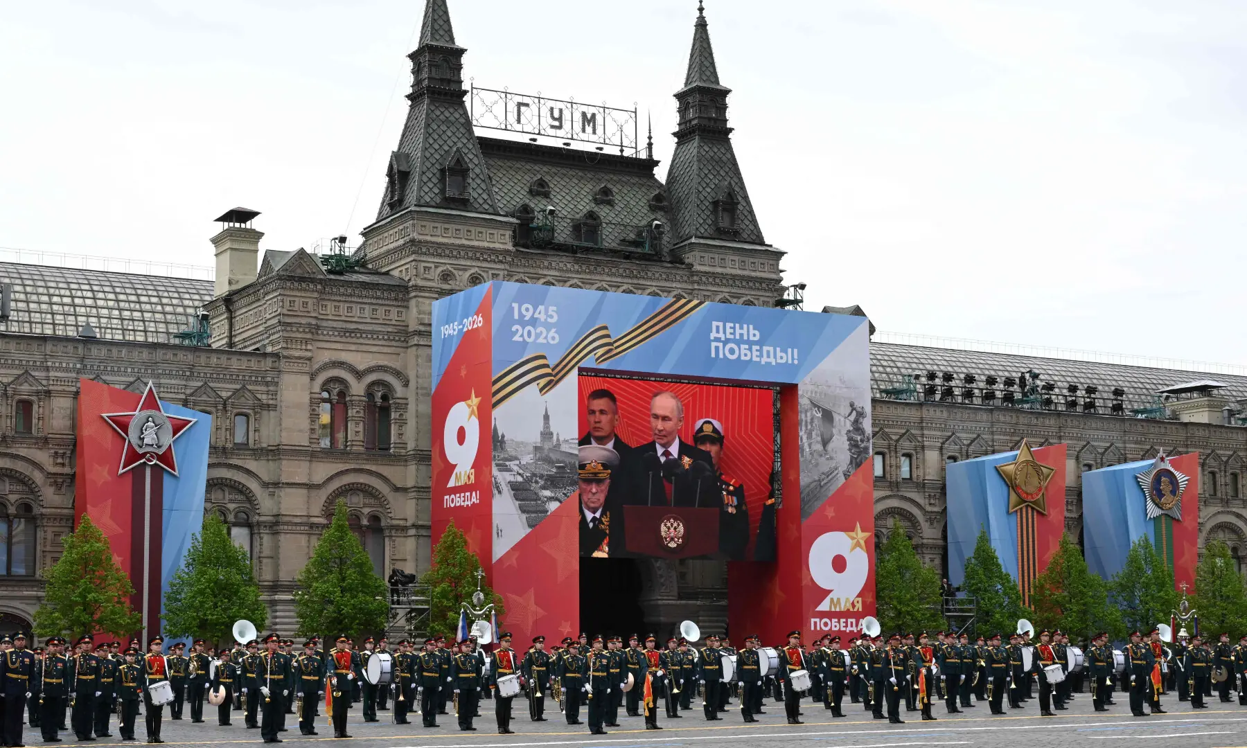 Members of a military band stand next to a screen broadcasting Russia's President Vladimir Putin's address during the Victory Day military parade in Moscow on May 9, 2026. &mdash; AFP