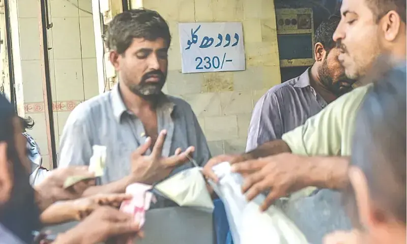 A retailer sells milk to customers as a pamphlet on the wall announces new prices of milk at a dairy shop in the Pakistan Chowk area in Karachi.&mdash;Fahim Siddiqi / White Star/File