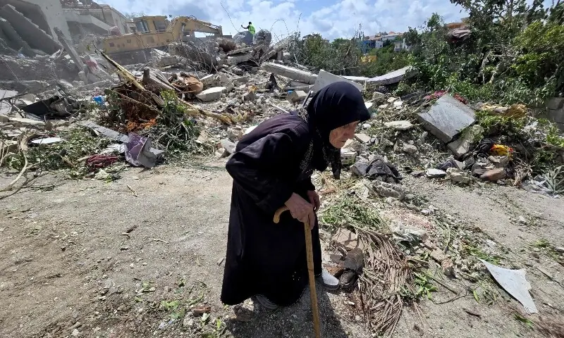 An elderly woman walks past Lebanese civil defence workers searching through the rubble in the southern Lebanese village of Deir Qanun al-Nahr on May 20, 2026. &mdash;AFP