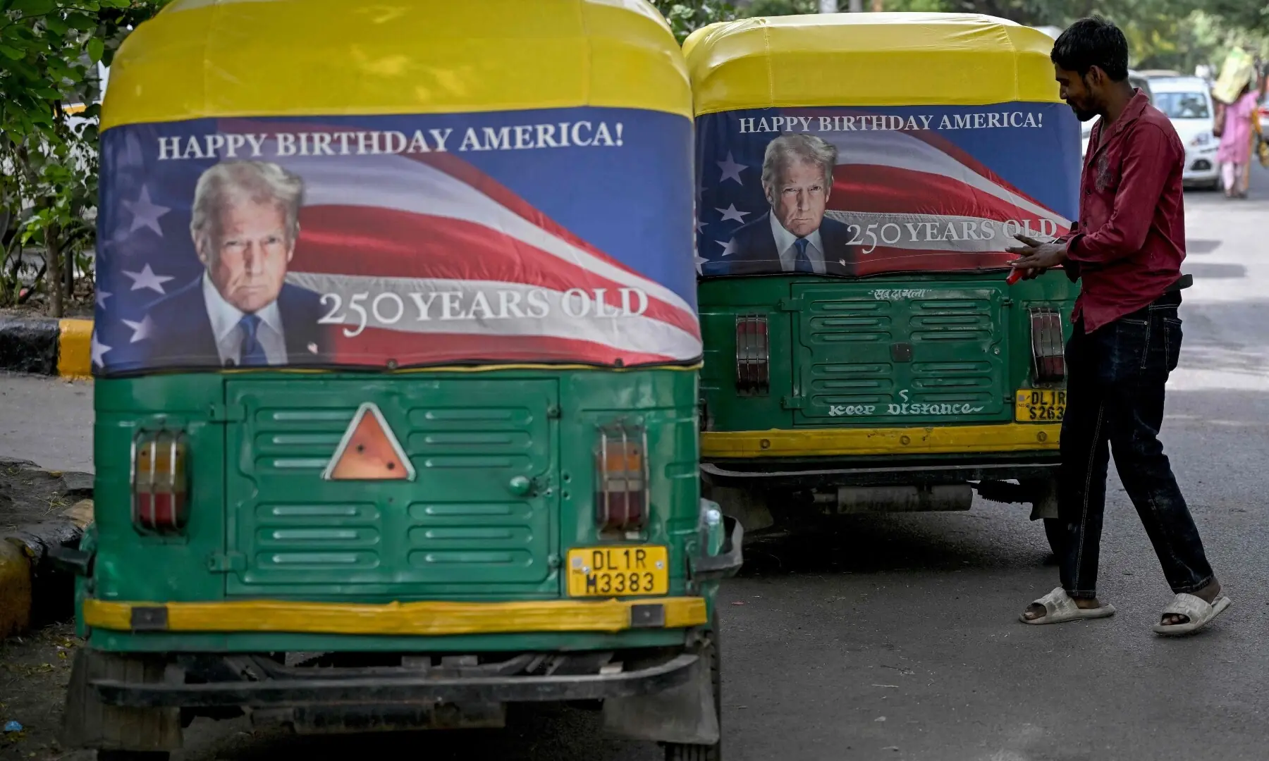A worker fixes a poster featuring US President Donald Trump on an autorickshaw in New Delhi on May 21, 2026 marking the 250th anniversary of American independence. — AFP