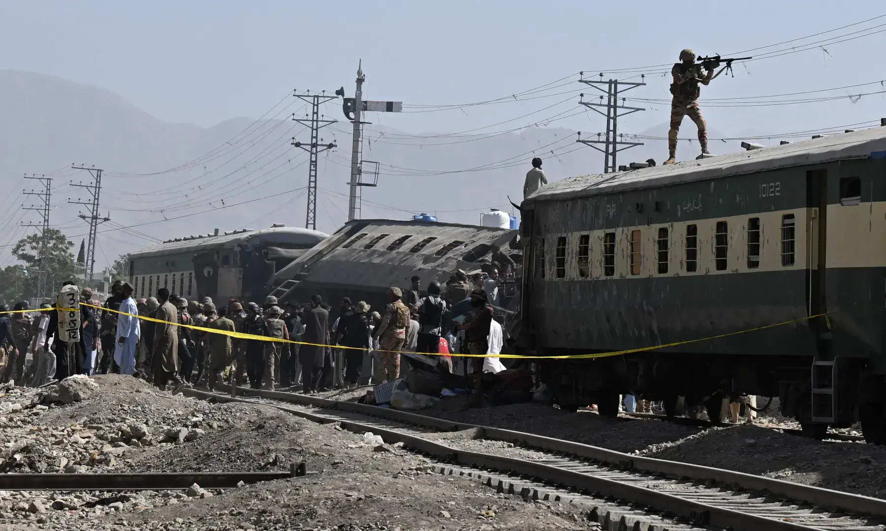 A soldier aims his weapon from atop a carriage as security officials inspect derailed train carriages after an explosion targeted a train in Quetta on May 24, 2026. &mdash; AFP