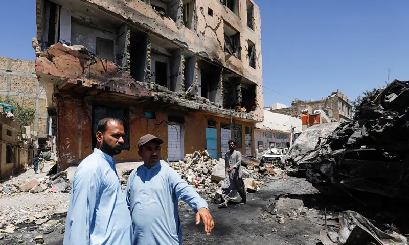 Residents stand next to a damaged building, rubble and destroyed cars a day after a blast near the Chaman railway crossing.&mdash;Reuters