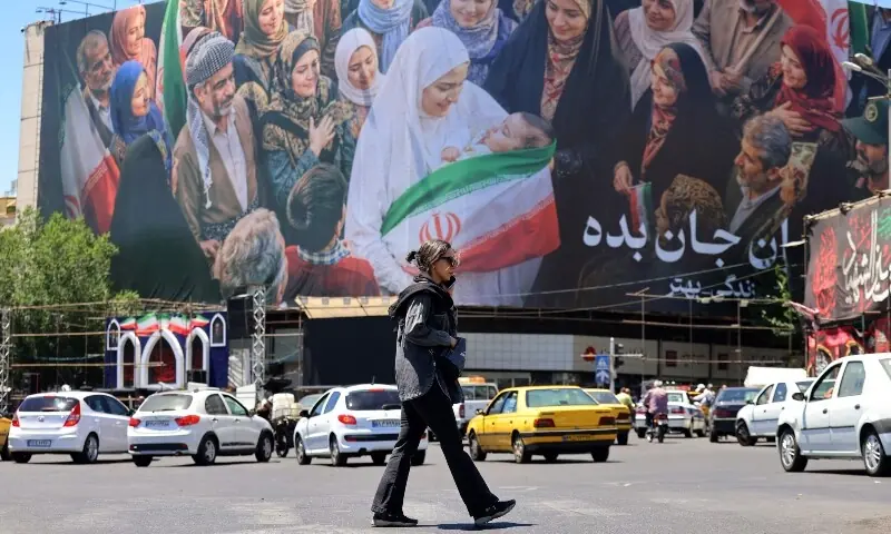 A woman crosses a street past vehicles moving near a large political billboard along Enghelab Square in central Tehran on May 26. &mdash; AFP