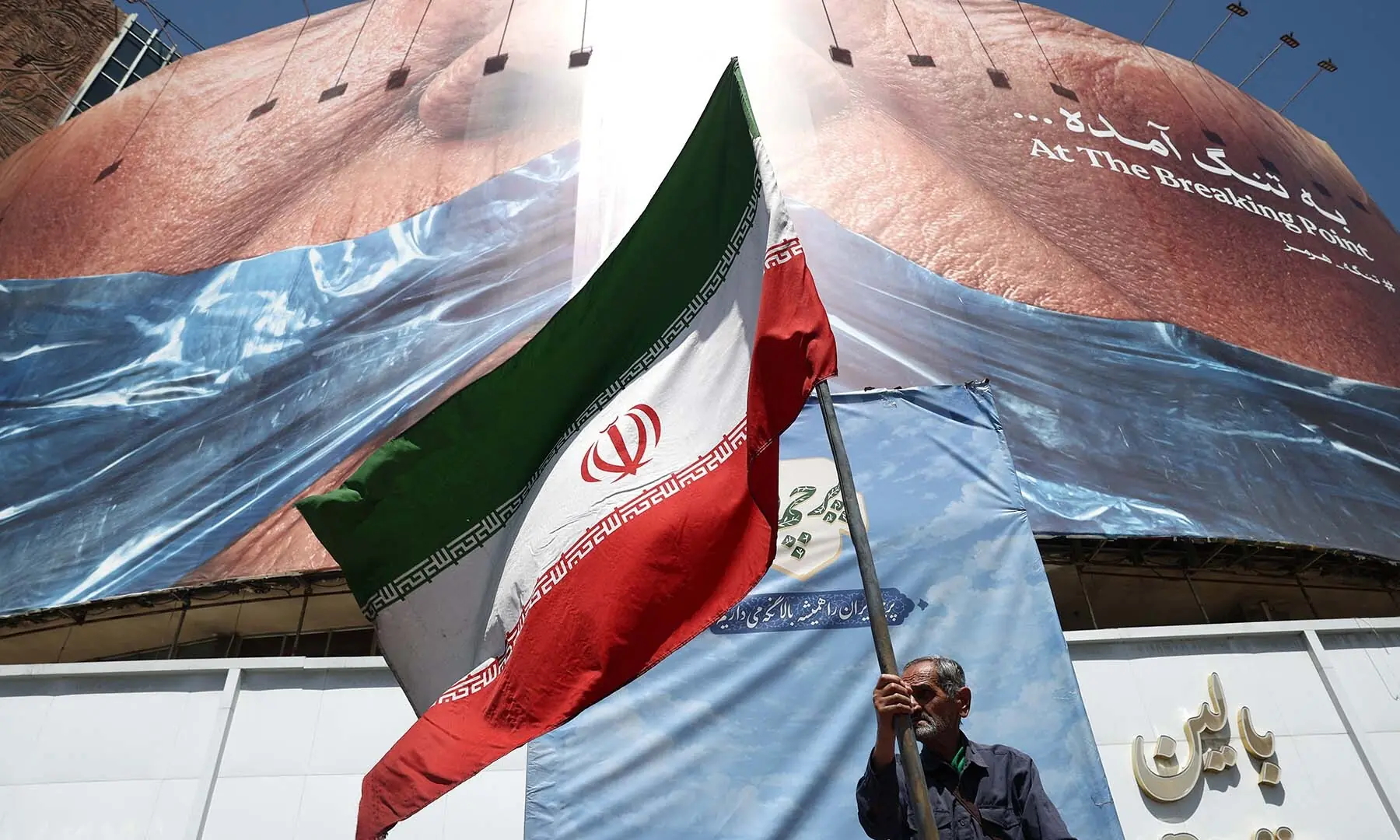 A man holds an Iranian flag near an anti-US billboard depicting President Donald Trump and the Strait of Hormuz, in Tehran, Iran on May 30, 2026. &mdash; Reuters