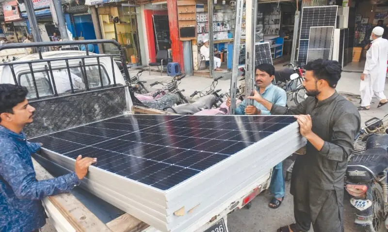Workers load solar panels onto a pickup for transportation to a site for installation.—White Star Workers load solar panels onto a pickup for transportation to a site for installation.—White Star