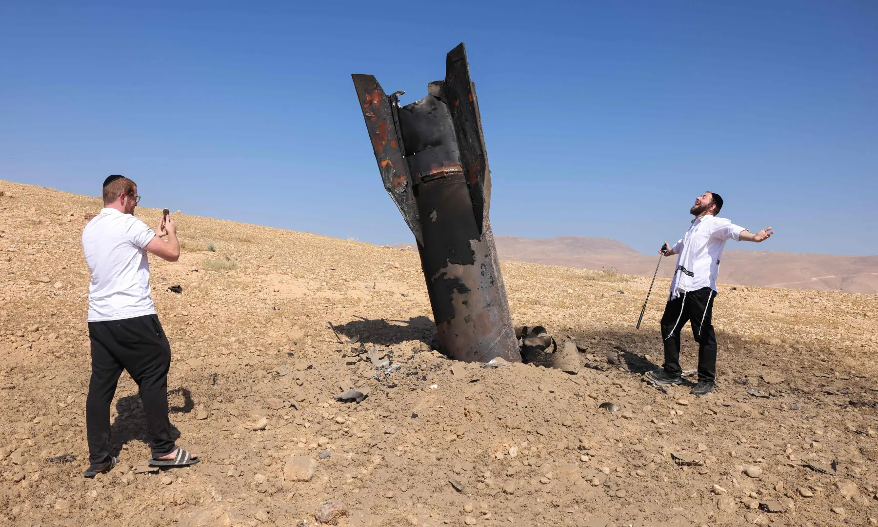  A man poses for a photo next to a fallen rocket half-buried in the ground on the outskirts of Jericho on June 8, 2026. &mdash; AFP 